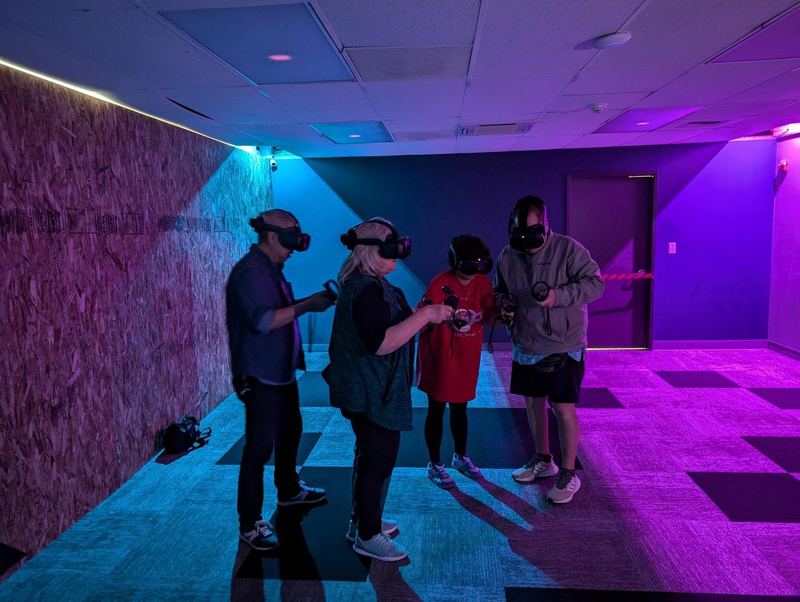 Four players in headsets play together in an arena lit purple and blue.