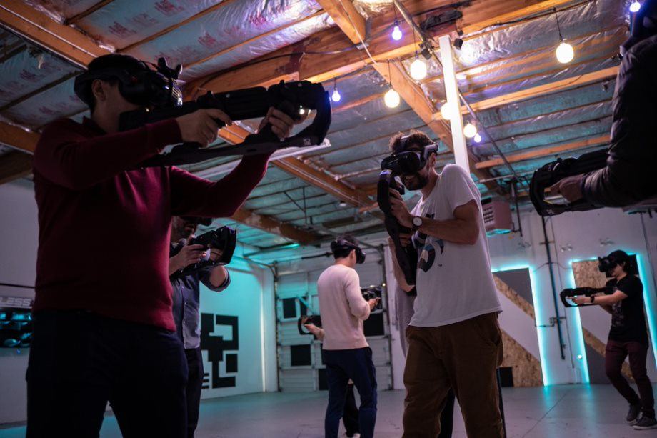 A team plays a shooter with VR blasters under string lights in the Tukwila arena.