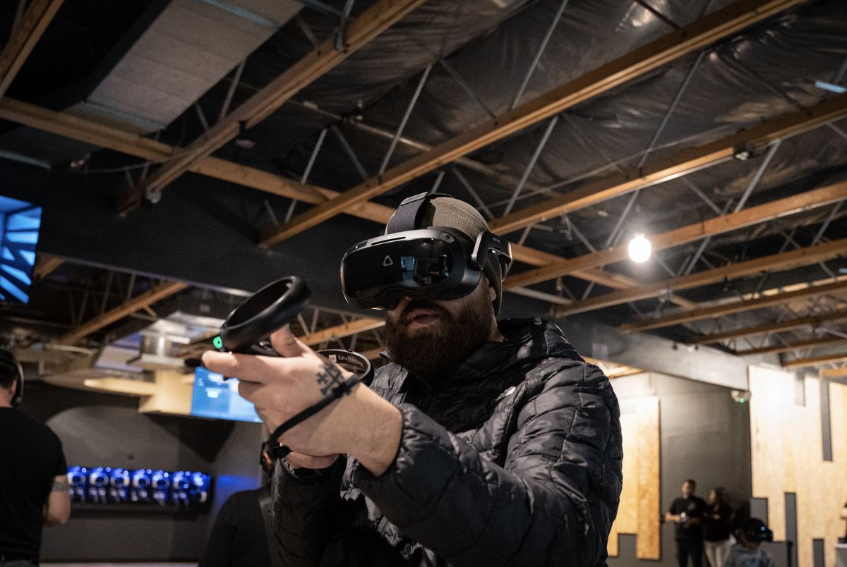 A player in a VR headset aims a controller in the Port Orchard arena, under exposed wooden roof beams.